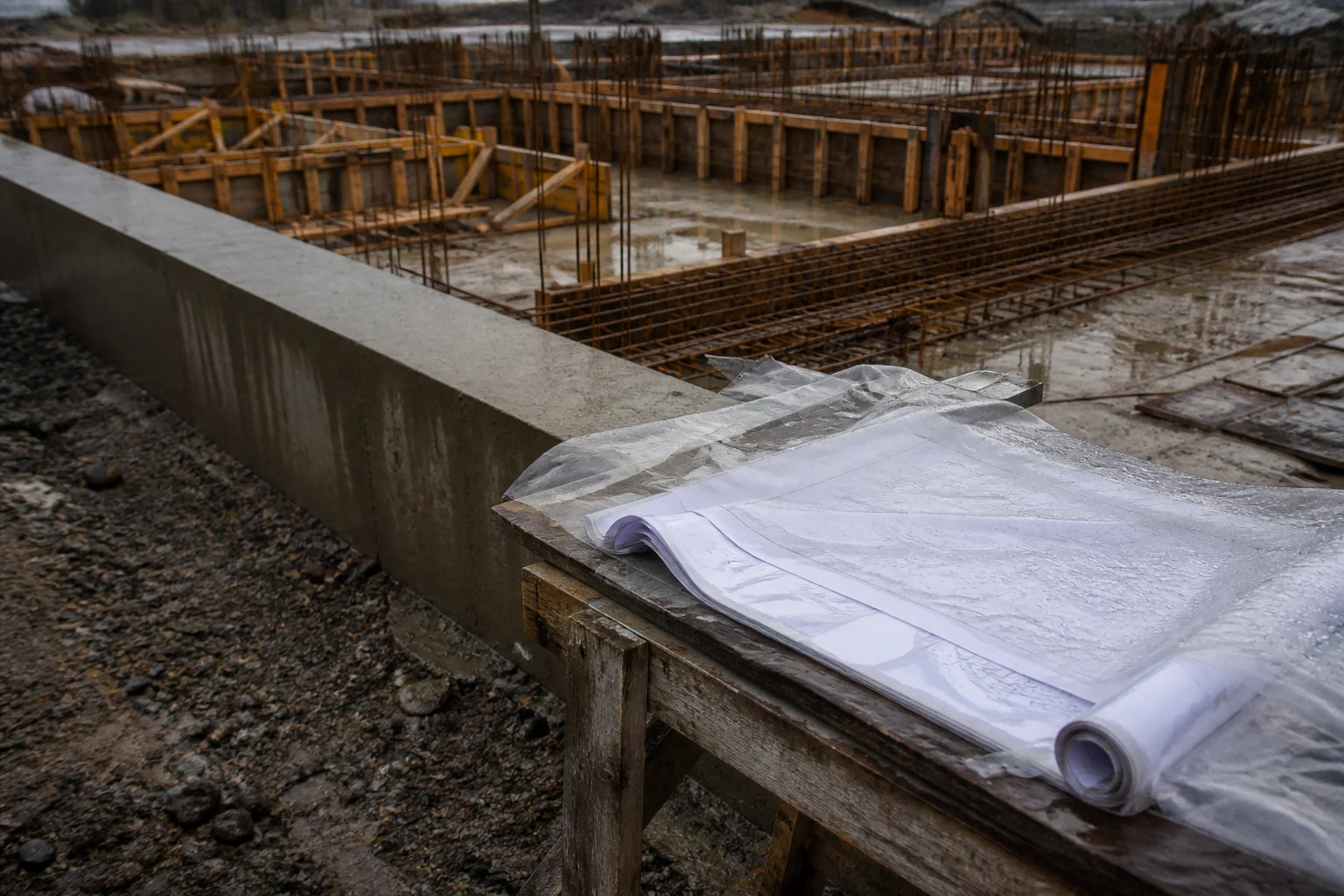 Generisk byggeplads med konstruktionstegninger, beton, forskalling og armering under udførelse.