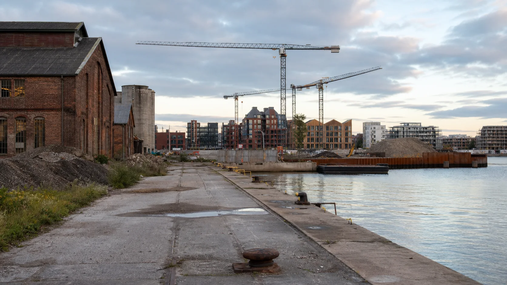 Bredt københavnsk havneområde med ældre industribygninger, kaj, kraner og nye bybygninger under opførelse.