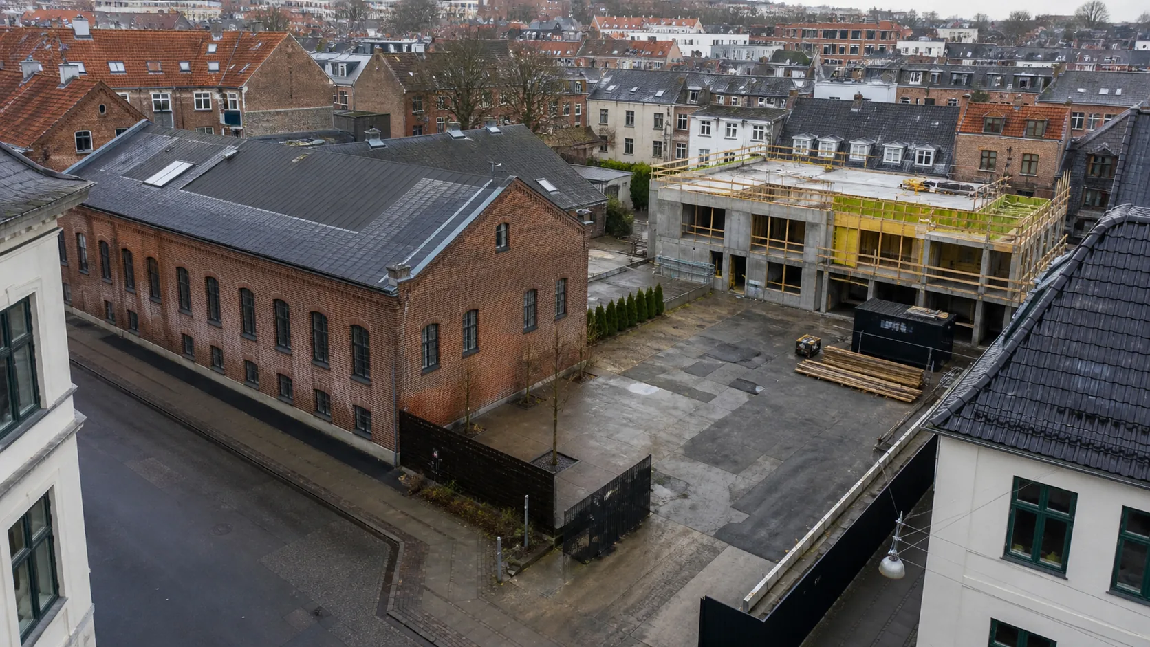 Københavnsk hjørneejendom med bevaret murstenshal, åbent gårdareal og ny beton- og trækonstruktion på en afgrænset del af grunden.
