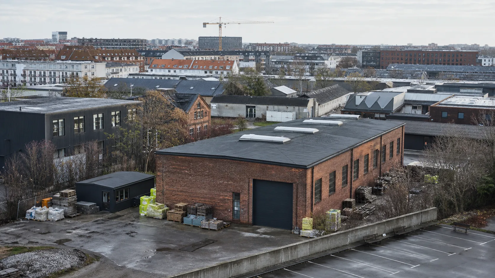 Bredt udsyn over et københavnsk erhvervsområde med en murstenshal og byggevarer i forgrunden samt mange forskellige ejendomme i baggrunden.