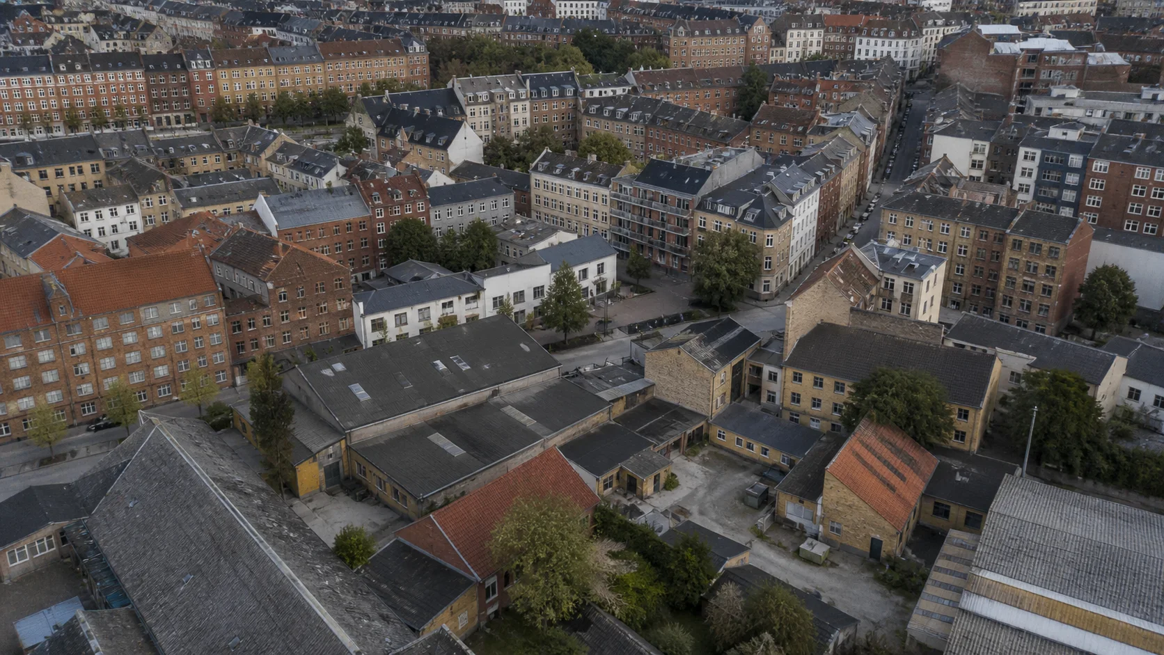 Skråt luftfoto over københavnsk overgangskvarter med uregelmæssige gader, gårdrum, industribygninger og tætte boligkarreer.