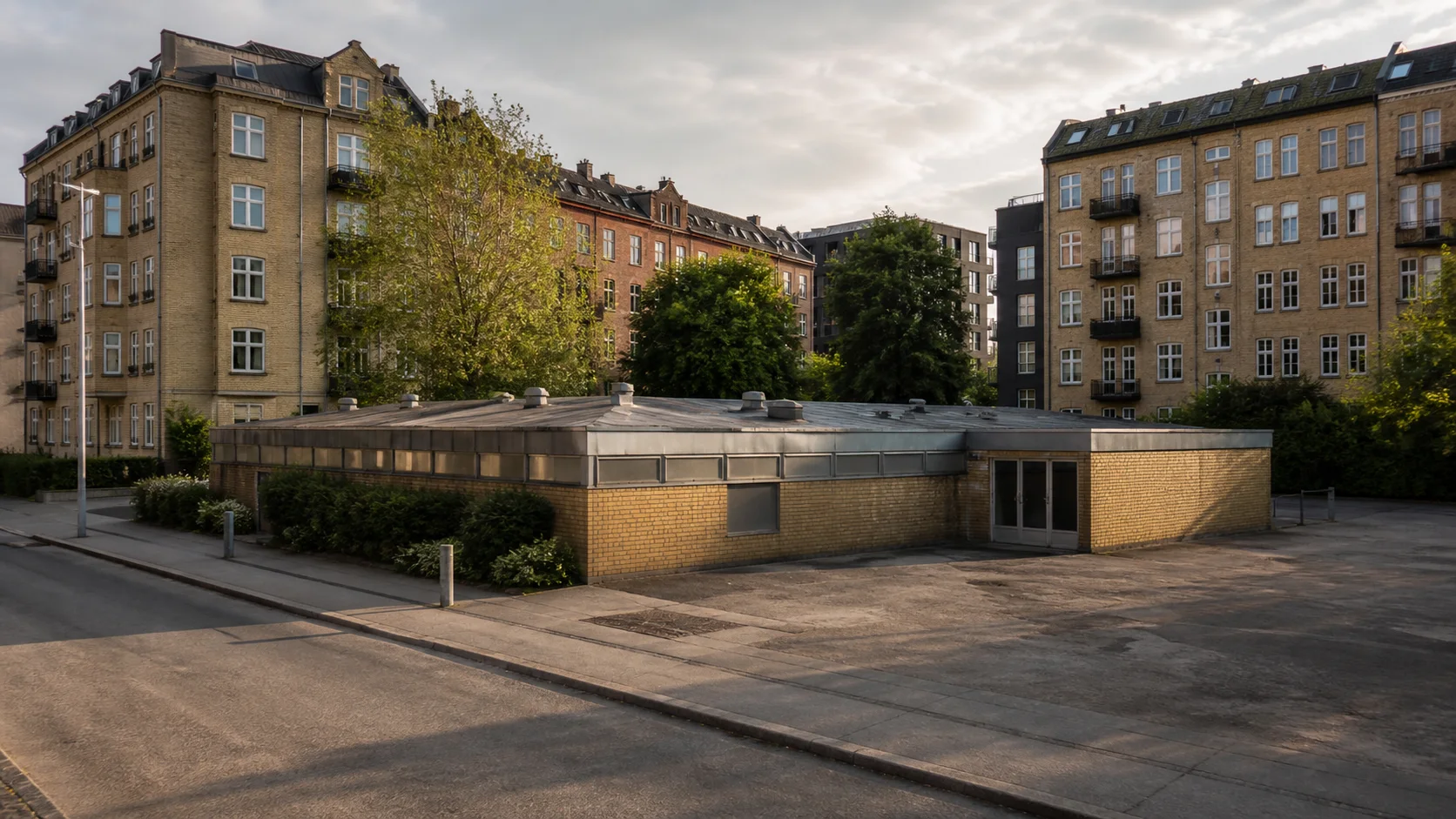 Lav gul murstensejendom på en åben københavnsk grund omgivet af højere boligkarreer.